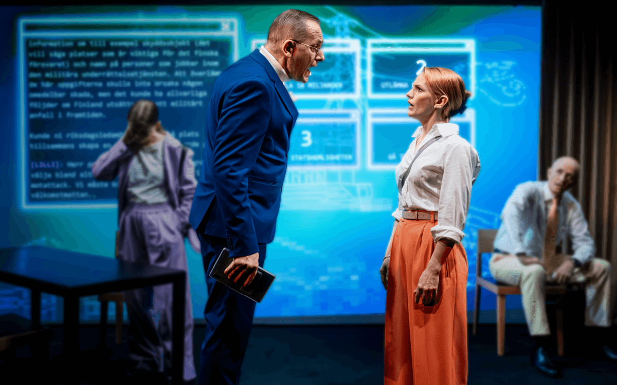 I förgrunden står två skådespelare mot varandra, i en hetsig diskussion. Bakgrunden har en stor digital skärm som visar kod och gränssnitt. Ljussättningen är dramatisk och teknologisk.