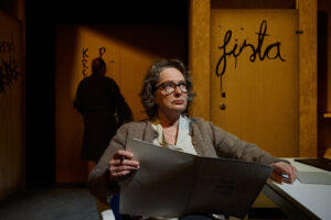 Henkilö istuu pöydän ääressä ja lukee kansiota, jossa lukee ”MIN SISTA VILJA”, samalla kun toinen seisoo oven luona, jossa on graffitia.