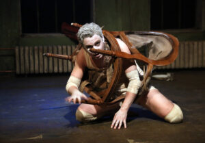 Förvandlingen av Kafka. I huvudrollen Patrick Henriksen. Han står på knä på golvet med huvudet igenom en stolsbotten. Han håller på att förvandlas till en insekt.