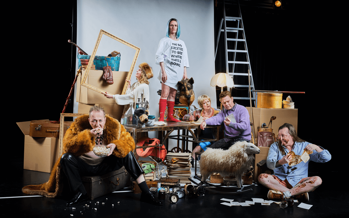 Skådespelarna i föreställningen Nattland i en teatralisk scen, omgiven av rekvisita, kartonger och möbler.
