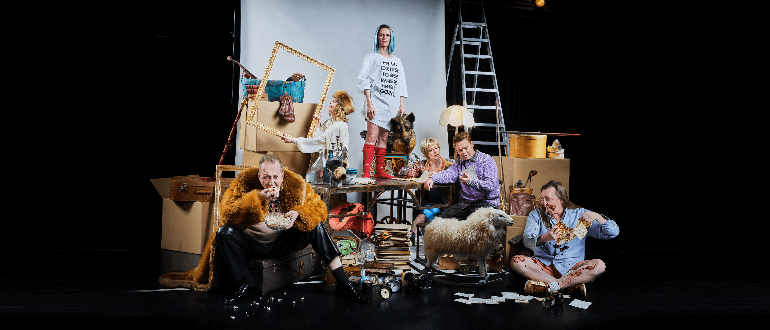 Skådespelarna i föreställningen Nattland i en teatralisk scen, omgiven av rekvisita, kartonger och möbler.